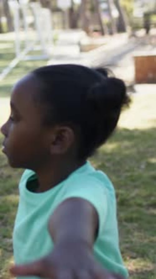 Camiseta de menina em pé com menta estendendo os braços, mão da segunda criança estendendo a mão sobre um tapete escuro no parque