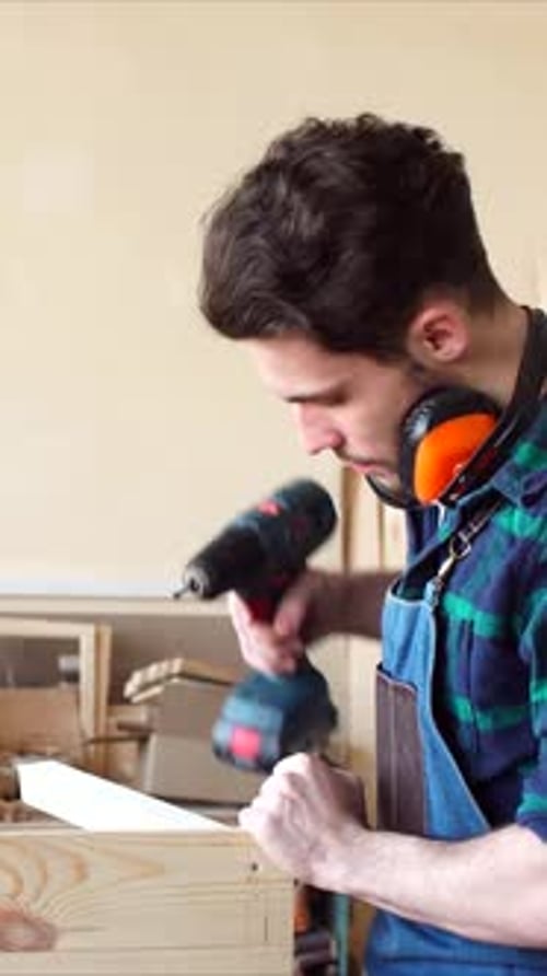 Young Man Drilling Wood Plank in Workshop