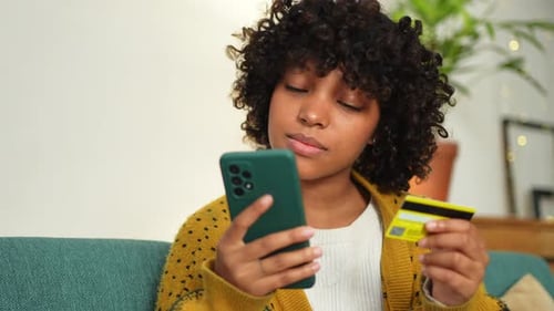 African American Woman Shopping Online Holding Smartphone Paying with Gold Credit Card Girl Sitting