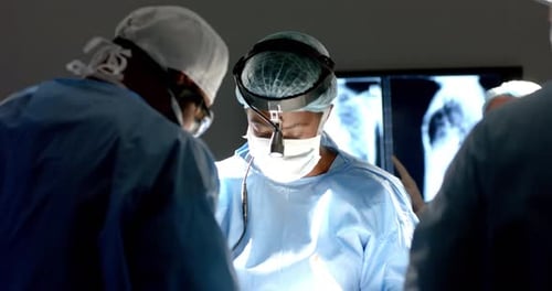 Diverse surgeons wearing surgical gowns operating on patient in operating theatre, slow motion