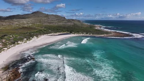 Lovely scenic aerial shot of a beach with rocky hills, sea green waters, lazy waves and partly cloud
