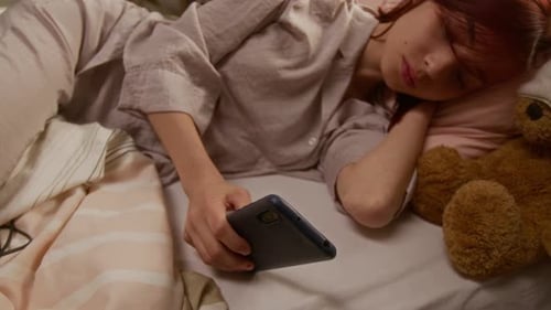 Young Woman Chilling in Bed, Scrolling Through Social Media