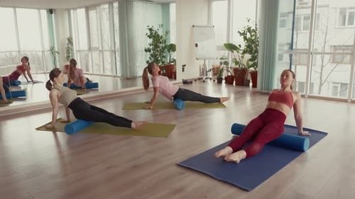 Three Women Using Foam Rollers for Fitness and Recovery Exercises in a Studio