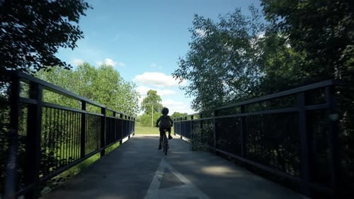 Following young boy on bicycle over bridge and paved trail, POV