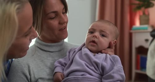 Lesbian couple holding their baby son sharing a tender moment at home in the USA