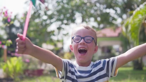 Boy in glasses is playing with pinwheel in a garden