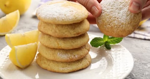 Mujer rompiendo una sabrosa galleta de limón en una mesa gris, primer plano