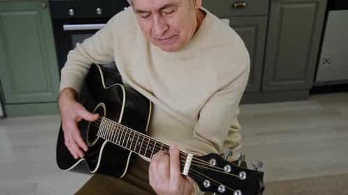 Senior Man Plays Acoustic Guitar in the Kitchen