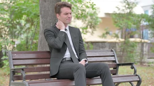 Man in Suit Rubs Neck on Park Bench