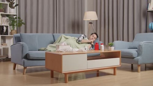 Homme asiatique avec une couverture souffrant de toux alors qu'il est allongé sur le canapé dans le salon à la maison