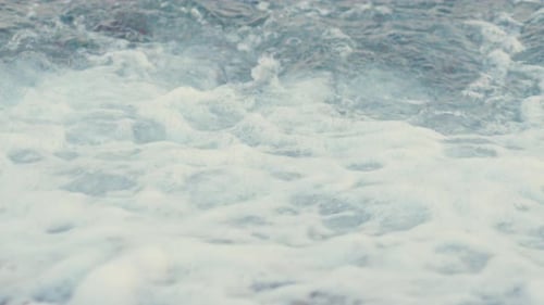 Stunning 4k video of a rocky beach with foamy blue waves and multiple colour stones.