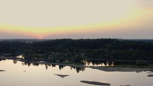 Flying towards sunset over the river. Aerial view overlooking the side of river bay.