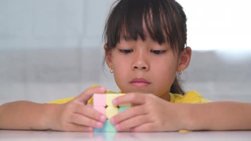 Girl Solving Pastel-Colored Cube Puzzle Indoors