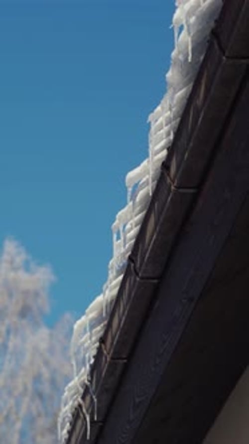 Frozen snow hanging over a roof. Vertical video of Icicles on a roof in a sunny and cold winter day.