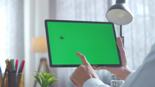 Close up of man's hand using a mock up green screen tablet on a desk at office