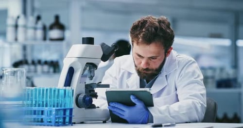 Scientist Using Microscope and Tablet in Lab