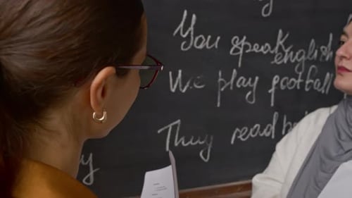 English Teacher Giving Lesson to Muslim Student in Front of Chalkboard
