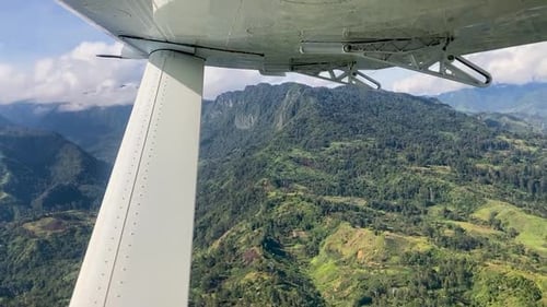 Wing of small airplane flying over rugged green mountains, Papua New Guinea