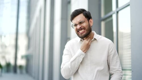Sick businessman suffering from a sore throat while standing on the street near a business office