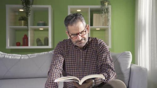 Man Reading Book Indoors on a Comfortable Sofa