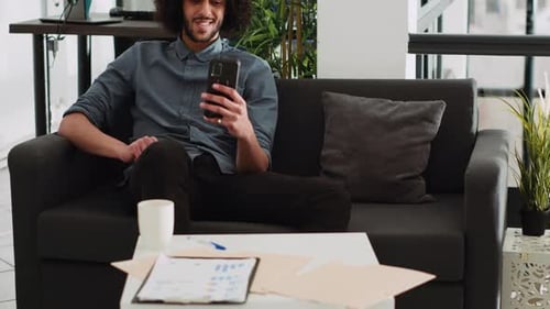 Young Adult Using Phone Relaxing on Sofa in Office