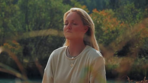 Kippaufnahme einer jungen Frau, die draußen an einem Bergsee meditiert. Sie atmet langsam.