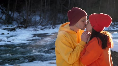A Caring Loving Man Warms the Hands of His Beloved Wife Near a Mountain River