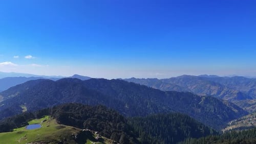 drone shot of a mountain ridge covered in dense forest under a clear, open sky
