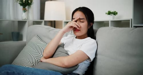 Sad Young Woman Sits on Couch with Pillow