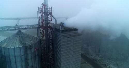 Grain processing plant premises on gray foggy day.