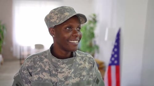 Smiling woman in army uniform indoors near flag