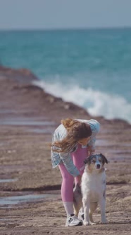 Affectionate Young Woman Caressing Australian Shepherd on a Rocky Beach