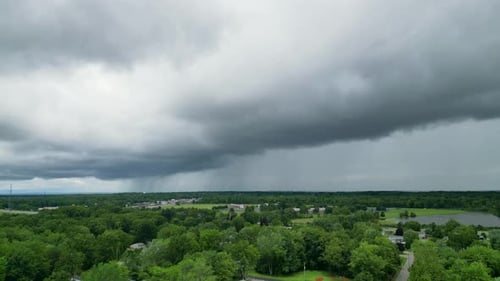 Drone shot of ominous storm clouds rolling over a suburban area with lush greenery below. Ideal for