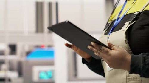 Un ingénieur d'une usine intelligente supervise les chaînes de montage robotiques à l'aide d'une application pour tablette