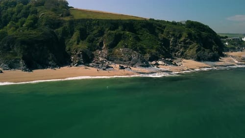Drone at sea travelling towards a sandy beach with cliffs behind. People are walking on the beach. G