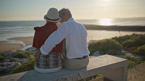 Elderly Couple Embracing on Bench at Sunset By the Ocean