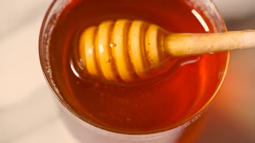 Pingando mel do gotejador de madeira na jarra de vidro Derramando mel