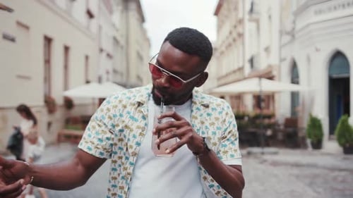Fabulous Young African Man in Cool Shirt Walking Down the Street with Lemonade in Hand Drinking