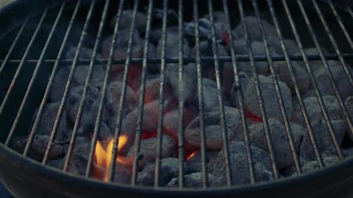 Extreme close-up shot of a brazier with grilling grate on and burning charcoal underneath