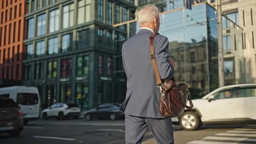 Un homme aux cheveux gris avec sac à bandoulière à bretelles marche sur la traversée