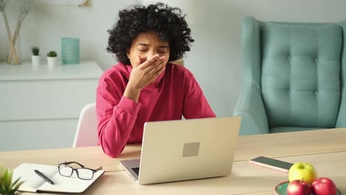 Sleepy African American Woman Sitting at Table with Laptop and Yawning