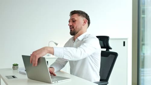 Businessman Finishes Work on Laptop Relaxes Stretches and Smiles in Office
