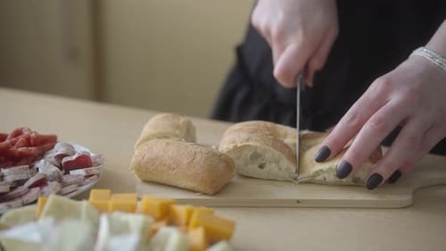 Hands Slice Baguette for Charcuterie Board Preparation