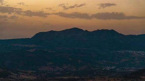 Sonnenuntergang in goldener Farbe über der Silhouette einer Bergkette mit fliegenden Wolken
