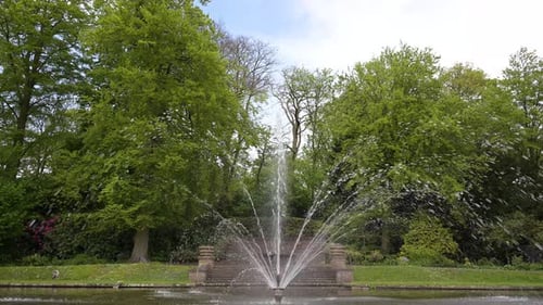 Ein laufender Springbrunnen inmitten eines ruhigen Wasserteichs unter blauem, bewölktem Himmel während des frühen Sprints