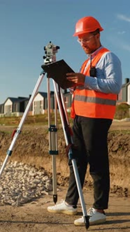 Surveyor Using Theodolite Inspects Construction Site on Sunny Day