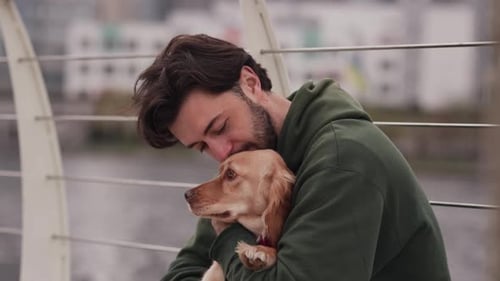 A Man Sits with His Dog on a Bridge with a Blurred River in the Background A Man with a Beard Hugs a