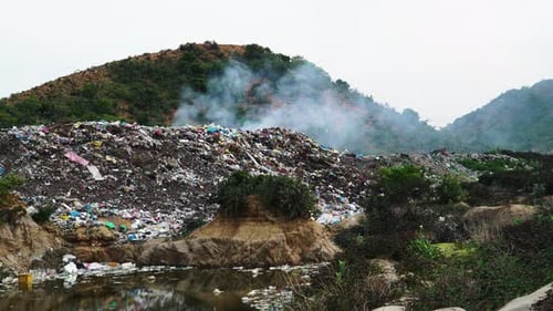 Close-up of heap of smoking rubbish in an open-air dump in middle of hill with sewage. Static view.