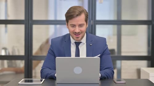Man Celebrates Success at Desk with Laptop