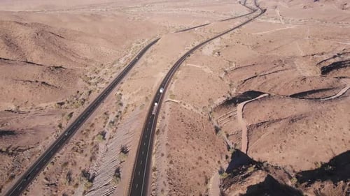 Vehicles travel on freeway in barren dry arid landscape and countryside, California, overhead aerial